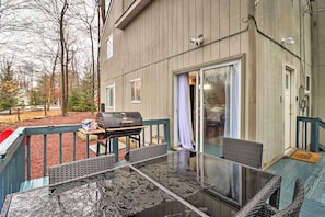 A covered outdoor patio with a glass table and wicker chairs, a barbecue grill, and a sliding glass door.