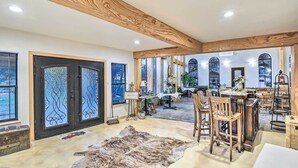 Une pièce spacieuse avec un grand plafond en bois, un tapis en fourrure, un coin repas avec des chaises en bois et une porte noire ornée de panneaux de verre décoratifs.