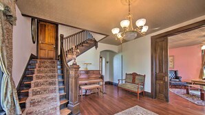 A grand staircase with a piano, a chandelier, and a large rug in a spacious living area. - Gettysburg Area Retreat, 12 Mi to Nat'l Park! (New Oxford)