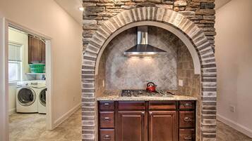 A kitchen with a stone archway, a stainless steel range hood, and a red kettle on the countertop.