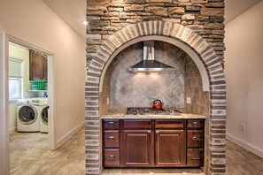 A kitchen with a stone archway, a stainless steel range hood, and a red kettle on the countertop.