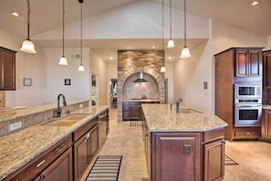 A spacious kitchen with granite countertops, a central island, and a stone fireplace.