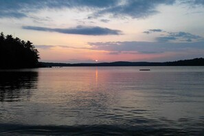 A calm lake at sunset with a boat in the foreground and a forested shoreline in the background. - 'the Cedars' Cabin w/ Beach Access on Panther Pond (Raymond)