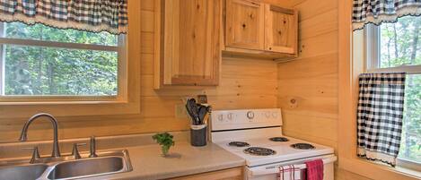 A kitchen with wooden cabinets, a white stove, a sink, and checkered window valances.