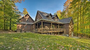A large wooden cabin with a covered porch and a deck, surrounded by a forest.
