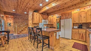 A wooden cabin-style kitchen with a central island, bar stools, a refrigerator, and a microwave.