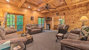 A cozy log cabin interior with a fireplace, leather sofas, and a dining area.