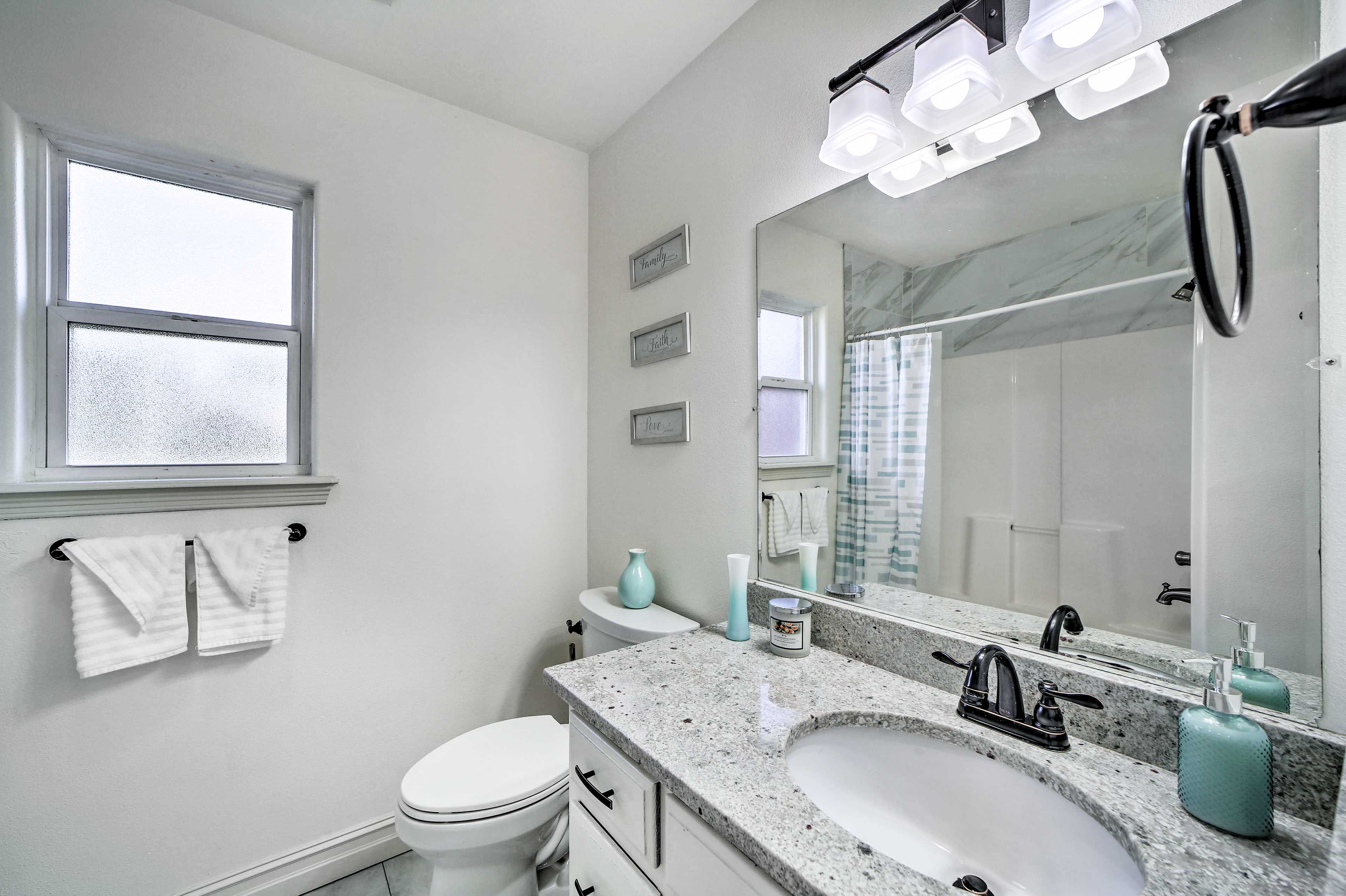 A bathroom with a white toilet, a sink with a mirror, and a window above the toilet.