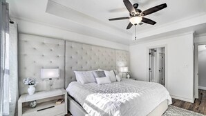 Une chambre à coucher avec une tête de lit capitonnée, une table de chevet avec une lampe, une commode et un tapis à motifs.
