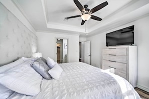 Een slaapkamer met een groot bed, een plafondventilator, een aan de muur bevestigde televisie en een houten dressoir.