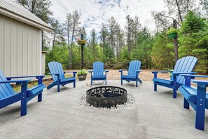 A fire pit surrounded by blue Adirondack chairs in an outdoor setting with a wooden building and trees in the background. - Walk to Castle Rock County Park: Rustic Cabin (Friendship)