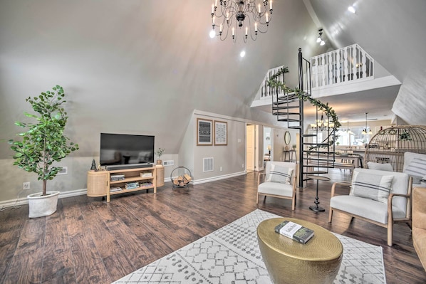 A spacious living room with a TV, comfortable seating, a staircase, and a decorative plant.