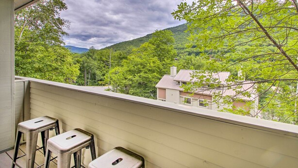 Un balcon avec deux tabourets et une vue sur un paysage verdoyant, avec des arbres et une colline.