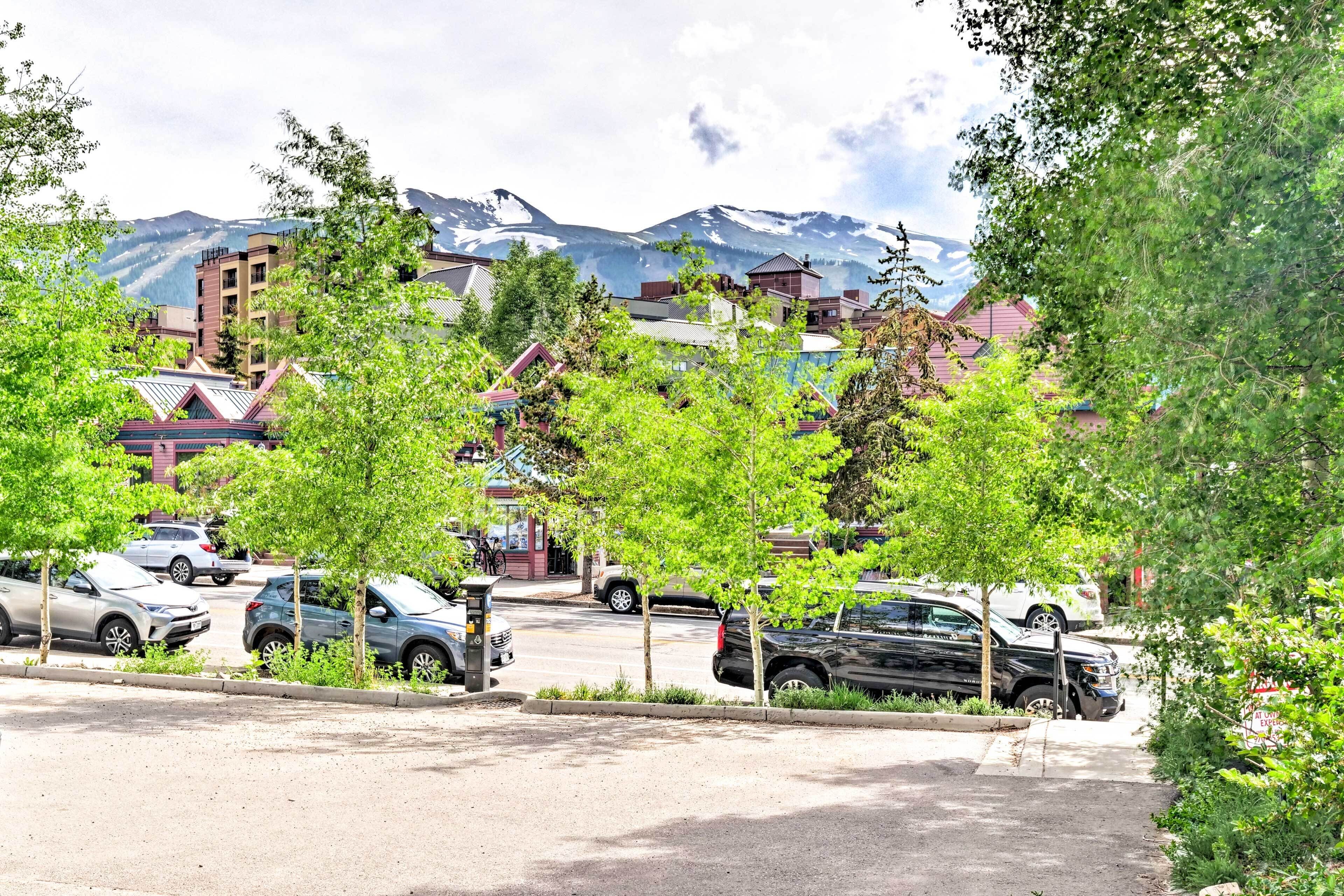 Ein Parkplatz mit mehreren Autos, umgeben von Bäumen und Gebäuden vor einer Bergkulisse.