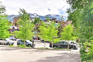 A parking lot with several cars, surrounded by trees and buildings with a mountain backdrop. - Walk to Slopes: Dtwn Breckenridge Condo on Main St (Breckenridge)