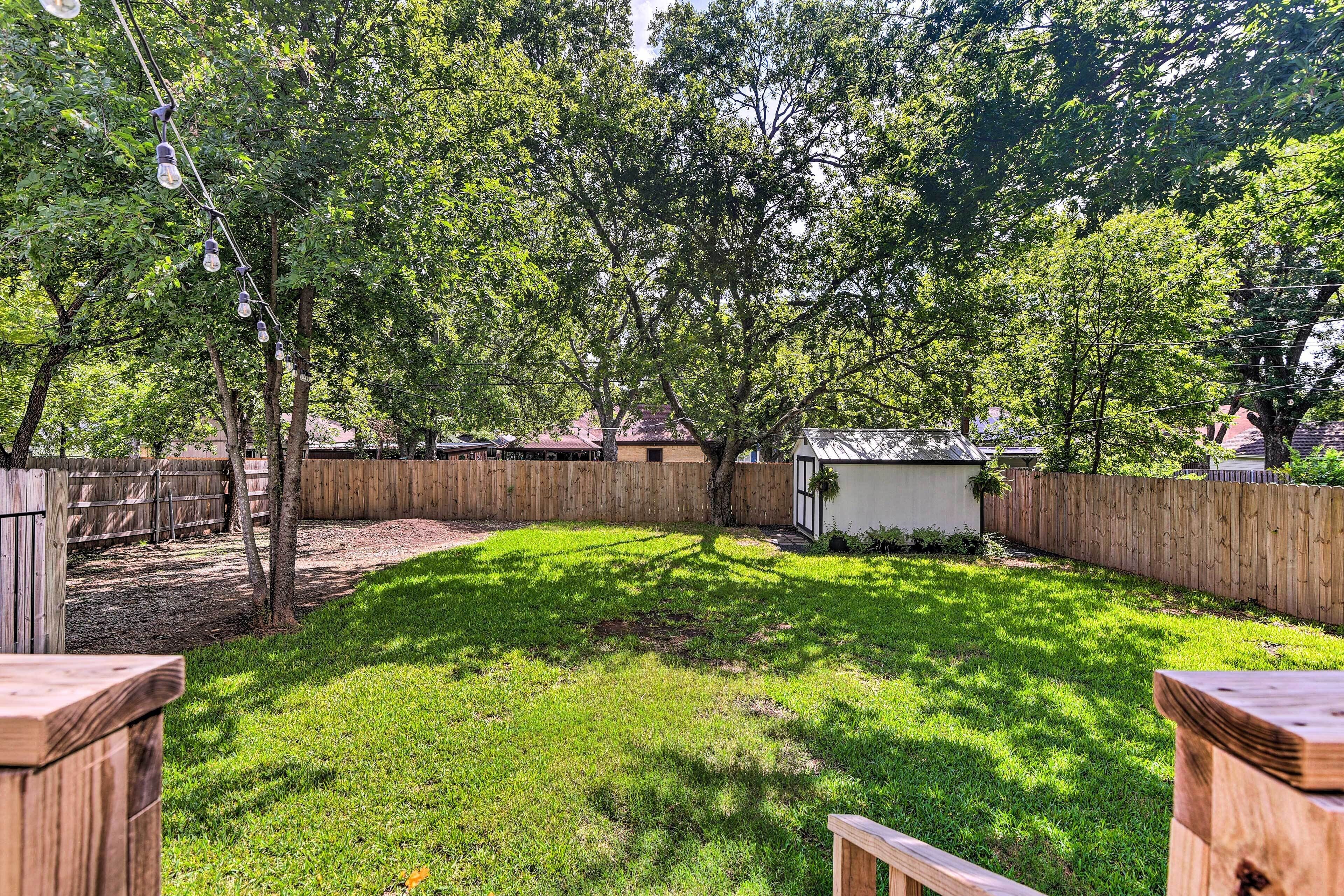 A backyard with a wooden fence, a small shed, and a tree.