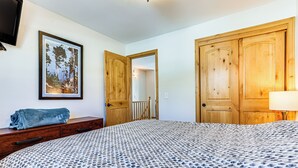 Une chambre à coucher avec une couvre-lit à motifs, une commode en bois, un tableau encadré au mur et des portes en bois.