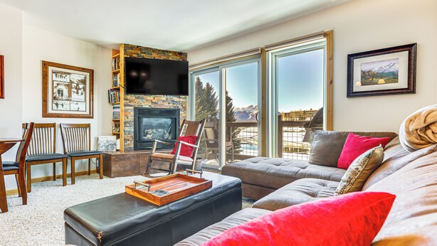 Un salon avec une cheminée, un canapé, une table basse et une vue sur les montagnes grâce à de grandes fenêtres.