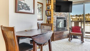 Un coin repas avec une table et des chaises en bois, une bibliothèque, une cheminée et un téléviseur fixé au mur.