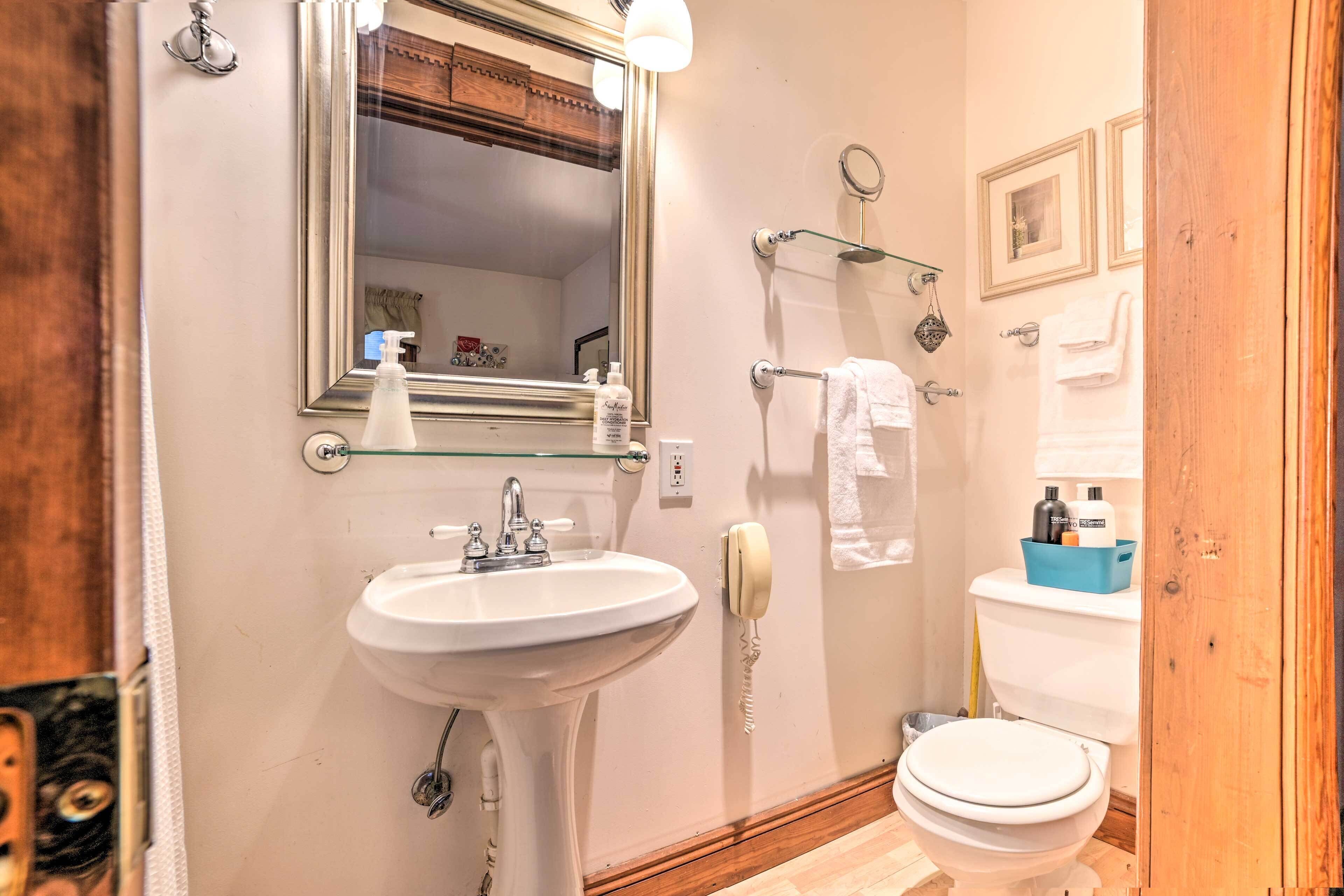 Une salle de bain avec un lavabo blanc, un miroir, des toilettes et une étagère en verre où sont rangés les articles de toilette.
