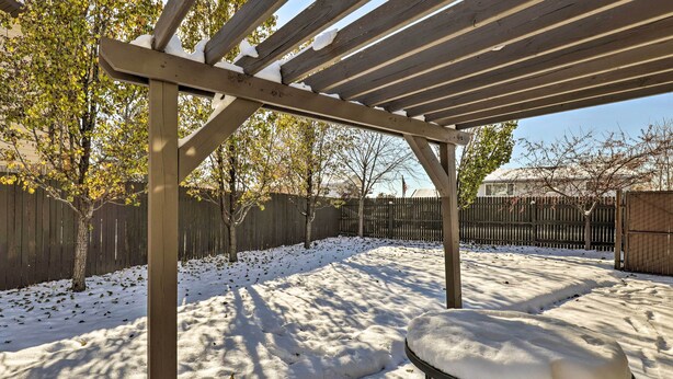 A covered patio area with a wooden pergola, a metal table with snow on top, and a snow-covered ground.