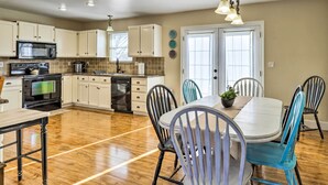 A modern kitchen with white cabinets, a microwave, stove, and dishwasher. There is a dining area with a white table and blue chairs.