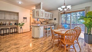 A kitchen with wooden flooring, white cabinets, a dining area with wooden chairs, and a large window with a view of trees. - 'lazy Bear Den' ~ 9 Mi to Vallecito Reservoir (Bayfield)