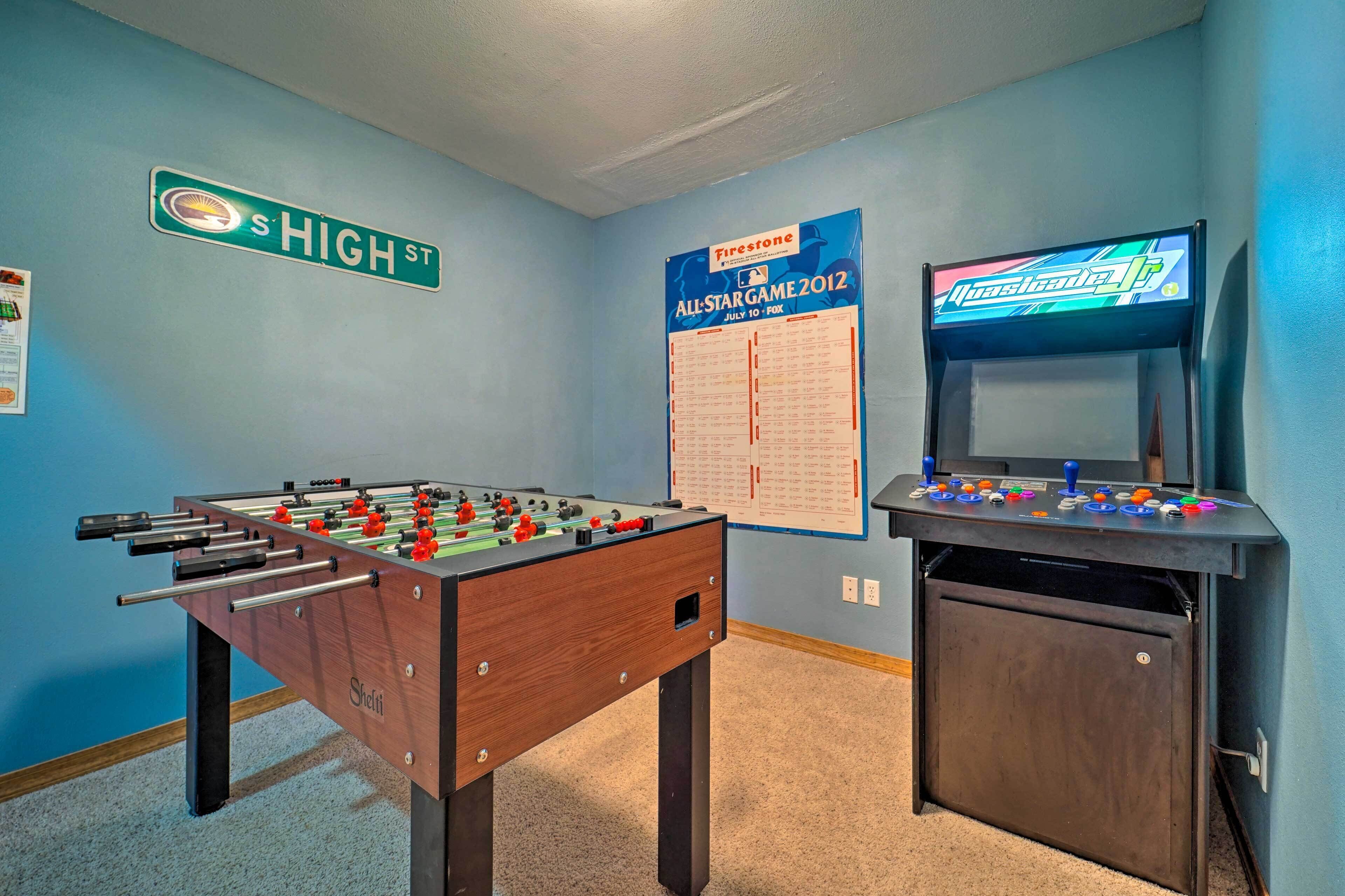 A room with a foosball table, a wall-mounted game console, and a poster for the All-Star Game 2012.