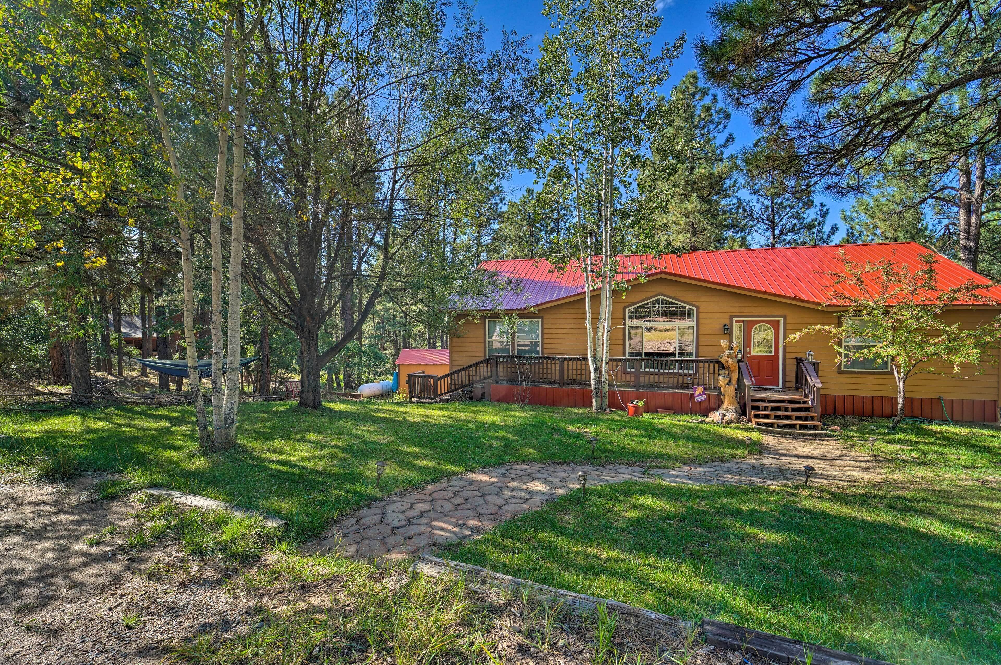 A yellow cabin with a red roof, surrounded by trees and a stone pathway leading to the entrance.