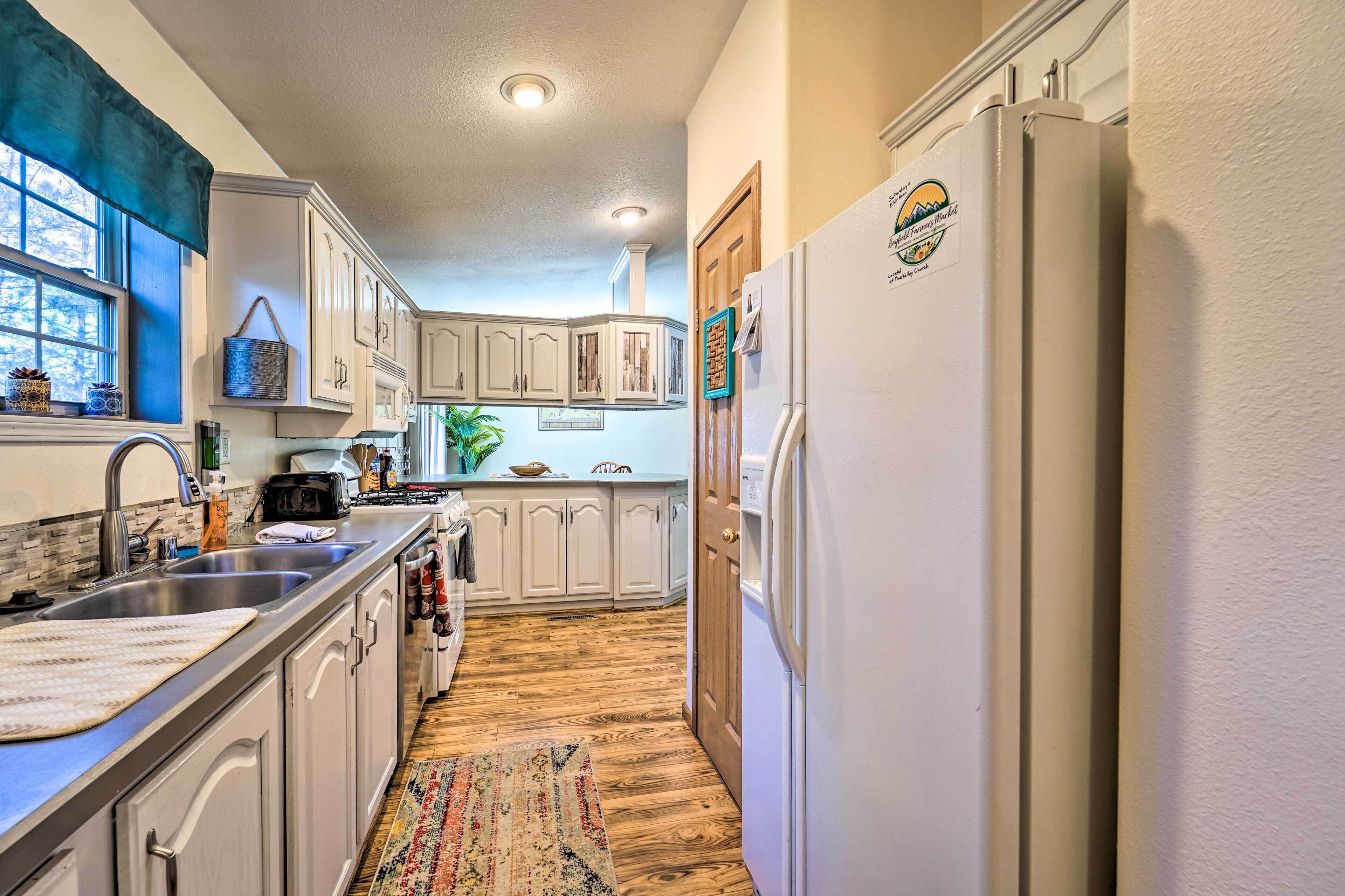 A narrow kitchen with white cabinets, a stainless steel sink, and a refrigerator with a logo.