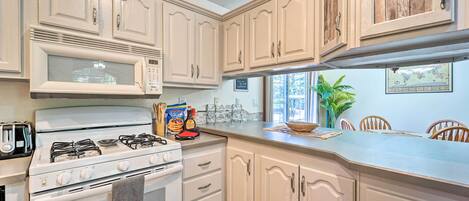 A kitchen with white cabinets, a stove, a microwave, and a window with a view of palm trees.
