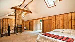 Ein Schlafzimmer mit Schlafgalerie, Holzwänden, einem Kamin aus Ziegelsteinen, einem Bett mit rot-schwarz kariertem Überwurf und einer Treppe mit Geländer.
