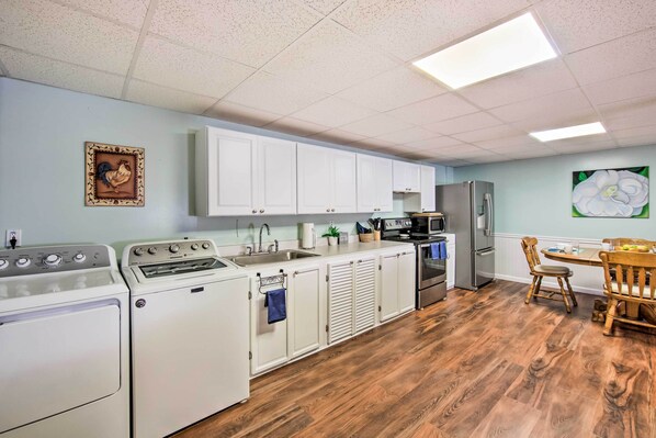 A kitchen with white cabinets, a sink, a stove, a refrigerator, and a dining area with wooden chairs.