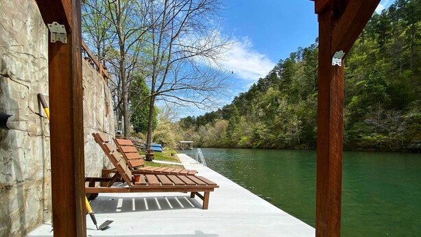 A wooden deck with lounge chairs overlooking a river, a stone wall, and a metal railing. - Home w/ Ouachita River & Lake Hamilton Access (Mountain Pine)