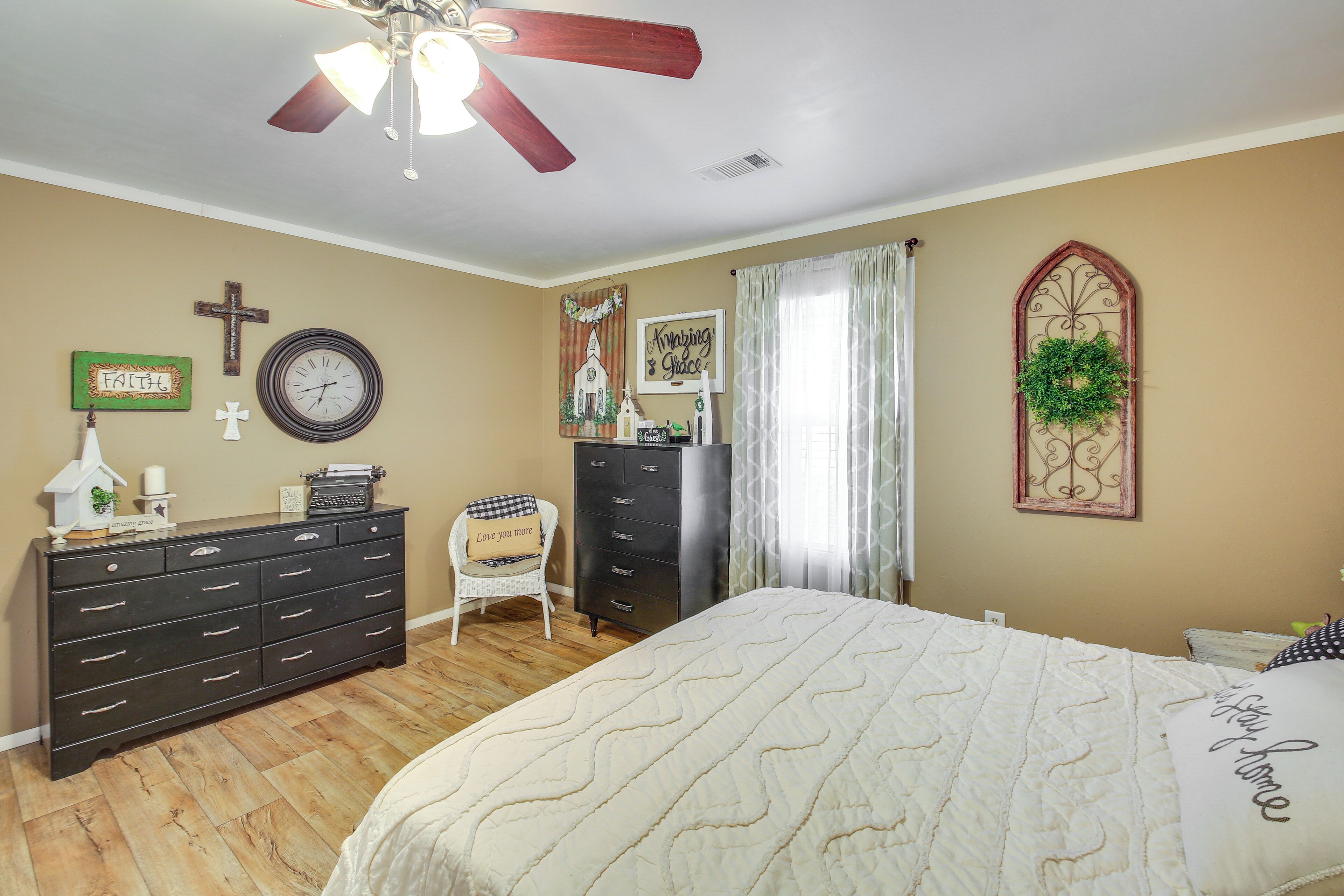 Une chambre à coucher avec un lit, une commode et une chaise. On y trouve une croix, une horloge et un élément de décoration murale.