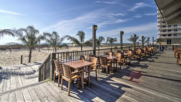 Una terraza de madera con mesas y sillas que da a una playa.