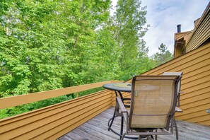 Eine Terrasse mit einem runden Tisch und einem Stuhl, umgeben von einem Holgitter, mit Blick auf einen üppigen, grünen Wald.
