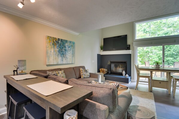 A modern living room with a sofa, coffee table, and fireplace. There is a dining area with a table and chairs. - Harbor Springs Condo ~ 6 Mi to Lake Michigan! (Harbor Springs)