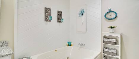 A bathroom with a white bathtub, a white shelf with baskets, a clock, and decorative wall panels.