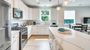 Una cocina moderna con armarios blancos, electrodomésticos de acero inoxidable, una isla grande e iluminación colgante.