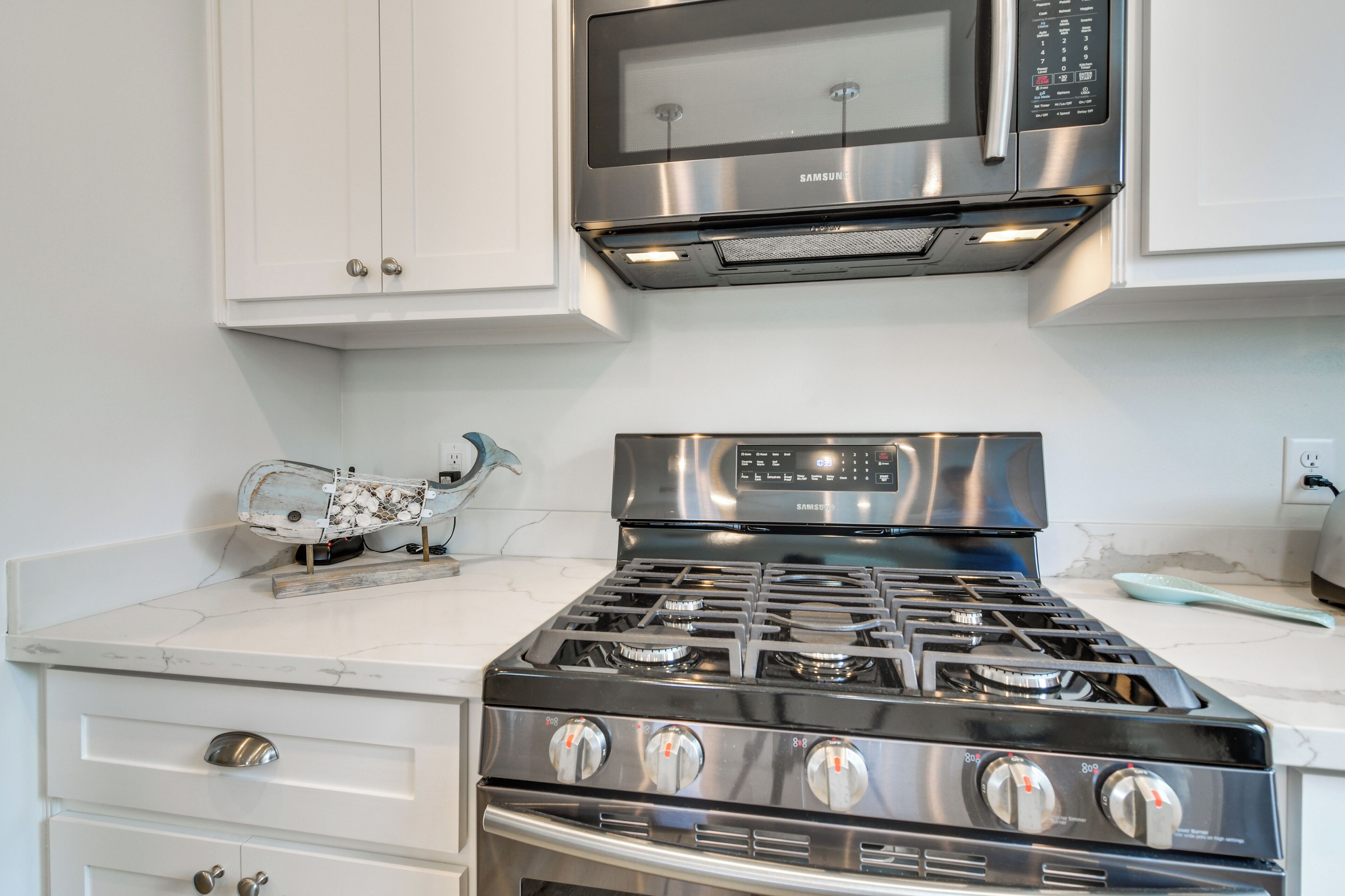 A kitchen with white cabinets, a stainless steel stove, and a microwave above it.