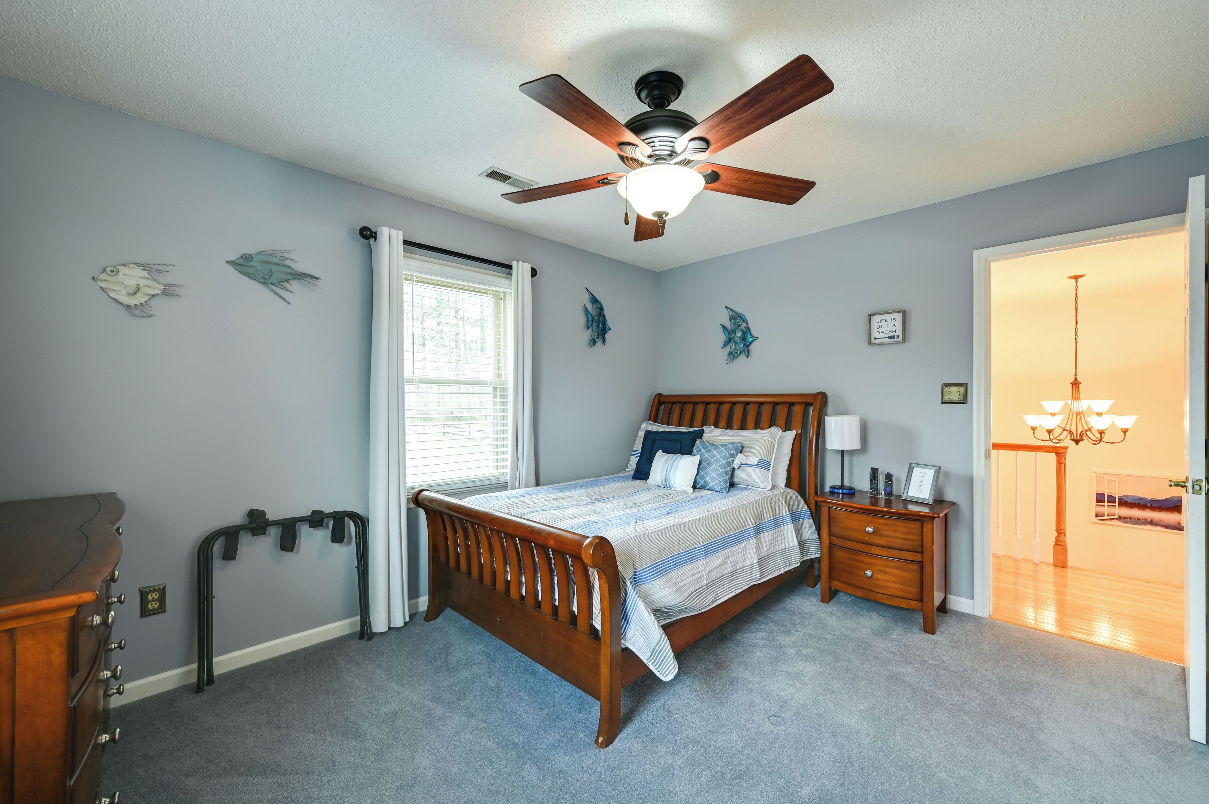A bedroom with a wooden bed, a ceiling fan, a nightstand, and a dresser.