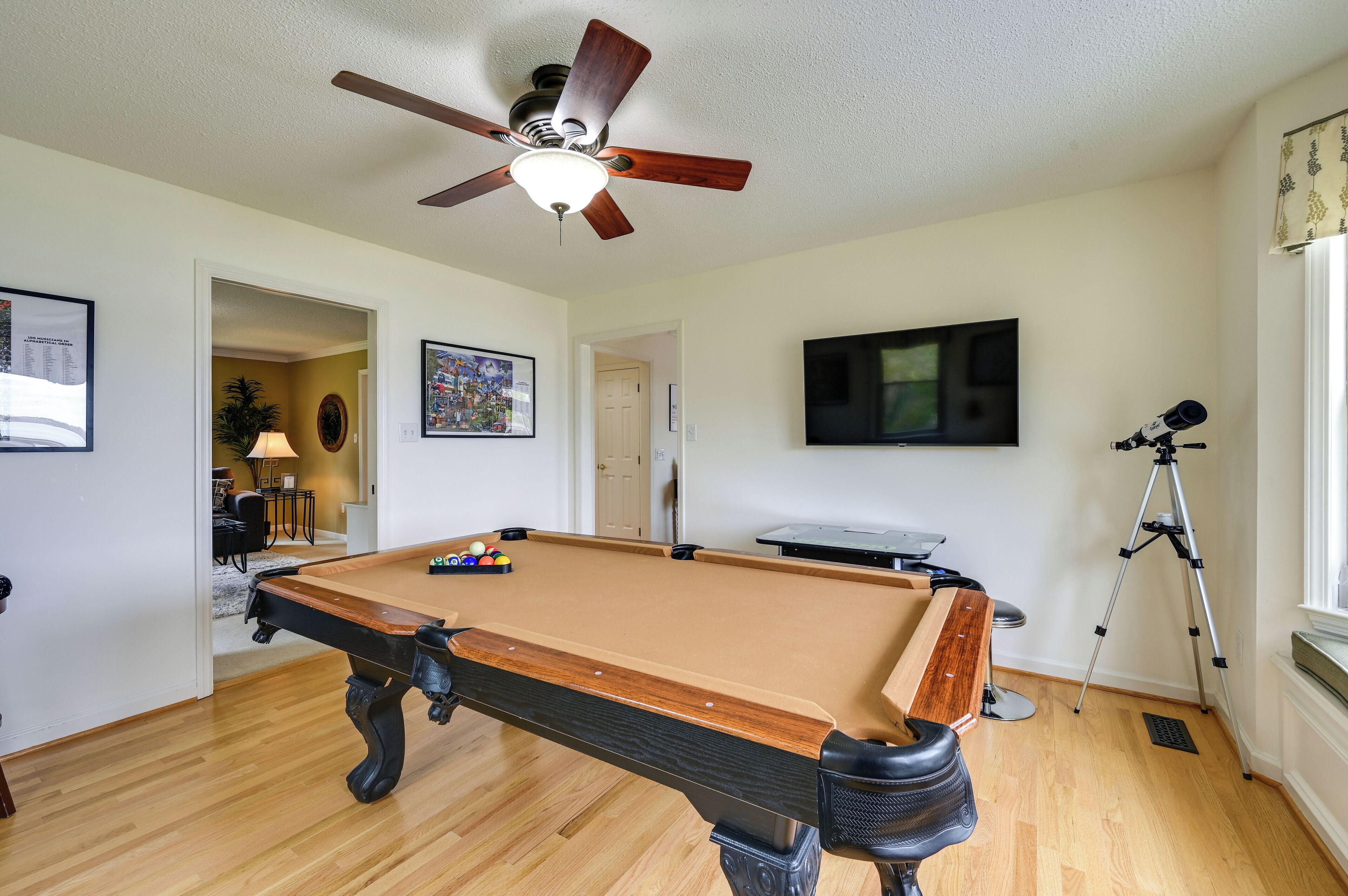 Une table de billard dans une pièce dotée d’un ventilateur de plafond, d’un téléviseur fixé au mur et d’un trépied.