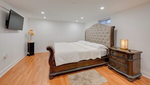A bedroom with a bed, dresser, TV, and a small window.