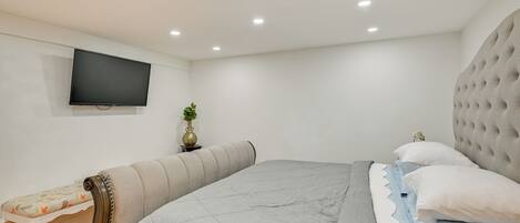 A bedroom with a bed, a bench, a television, and a wall-mounted plant.