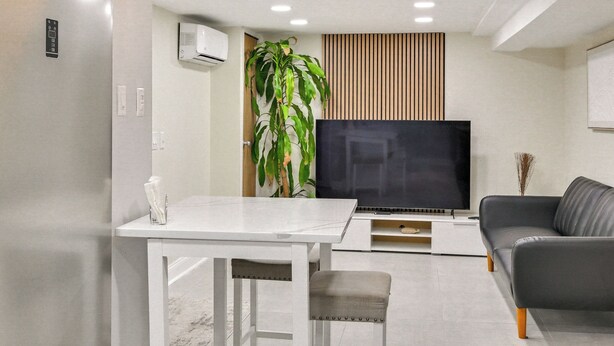 A modern living room with a white table, grey sofa, and a large flat-screen TV.