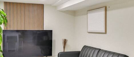 A modern living room with a flat-screen TV on a white entertainment unit, a grey leather sofa, and a wooden slat wall panel.