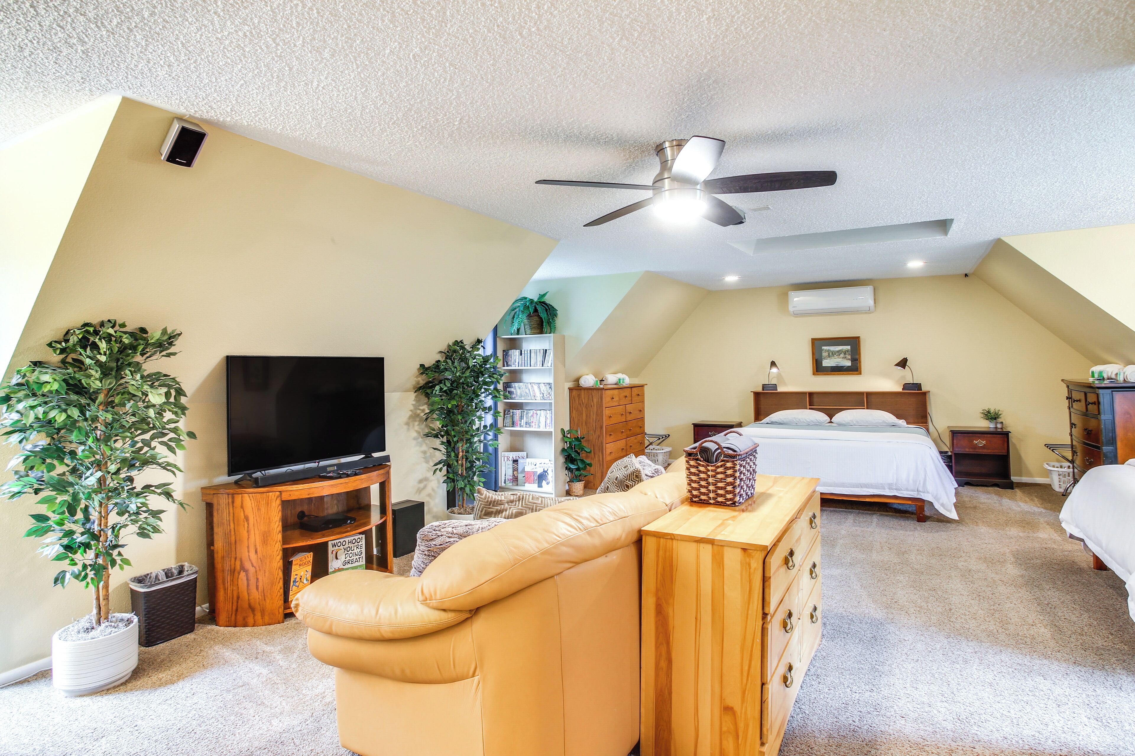 A bedroom with a bed, a TV, a ceiling fan, and a wooden dresser.