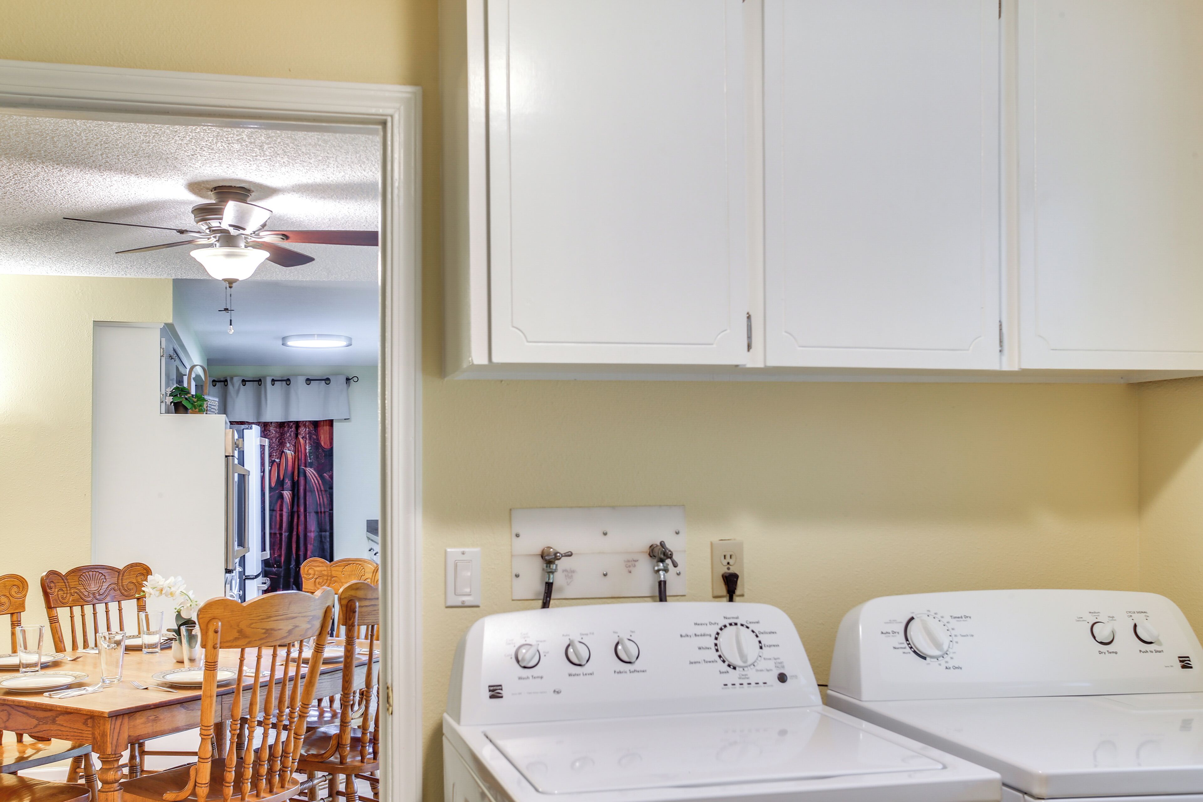 A laundry area with two white washing machines, a ceiling fan, and a dining area with wooden chairs and a table.