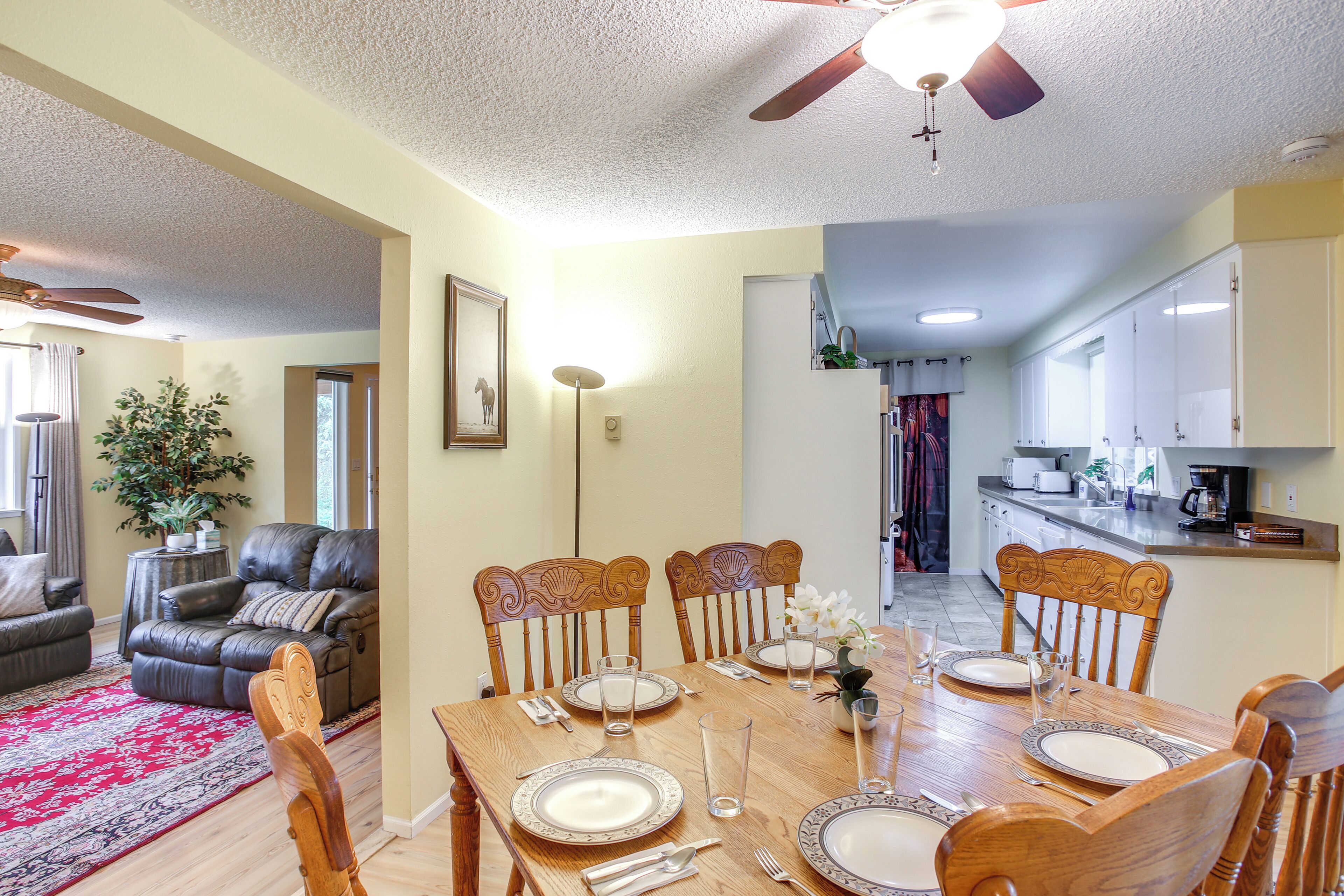 A dining area with a wooden table set for six, flanked by two leather sofas and a red patterned rug.